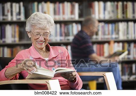 Stock Image - Caucasian woman reading book in library. Fotosearch