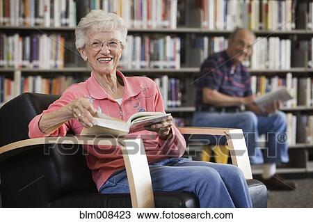 Stock Image - Caucasian woman reading book in library. Fotosearch