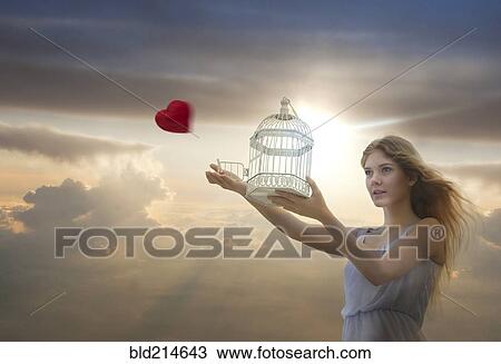 Stock Image - Caucasian woman releasing heart from birdcage. Fotosearch