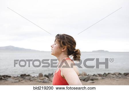 Stock Image - Caucasian woman resting on rocky beach. Fotosearch