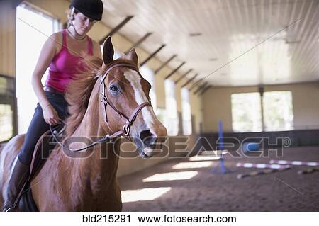 Stock Image - Caucasian woman riding horse in indoor paddock. Fotosearch
