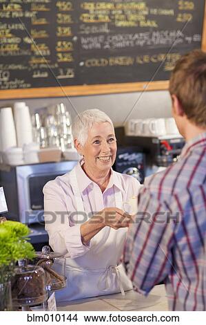 Picture - Caucasian woman serving customer coffee in cafe. Fotosearch