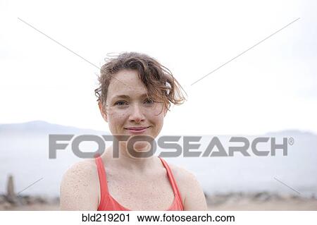 Stock Image - Caucasian woman smiling on rocky beach. Fotosearch