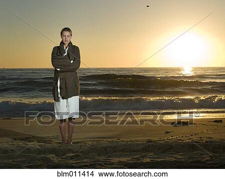 Picture - Caucasian woman standing on beach at sunset. Fotosearch
