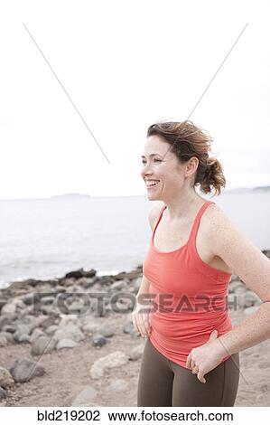 Stock Image - Caucasian woman standing on rocky beach. Fotosearch