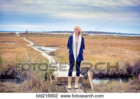 Stock Image - Caucasian woman standing on walkway in rural field. Fotosearch