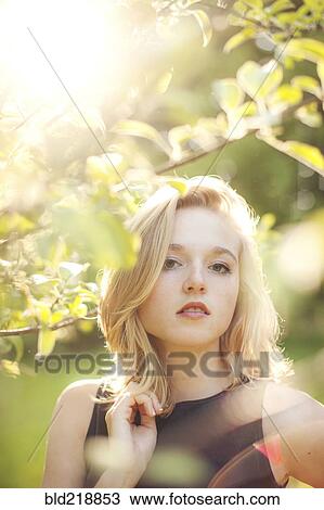 Stock Image - Caucasian woman standing under tree branches. Fotosearch