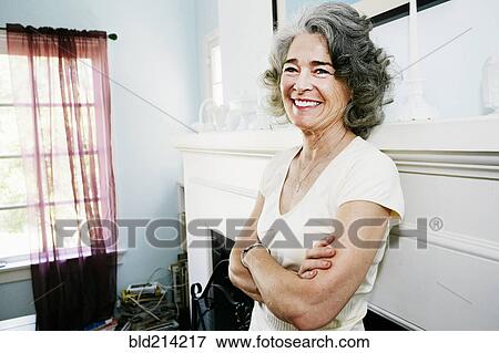 Stock Photo - Caucasian woman standing with arms crossed in living room. Fotosearch