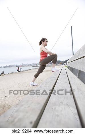 Picture - Caucasian woman stretching on beach bench. Fotosearch