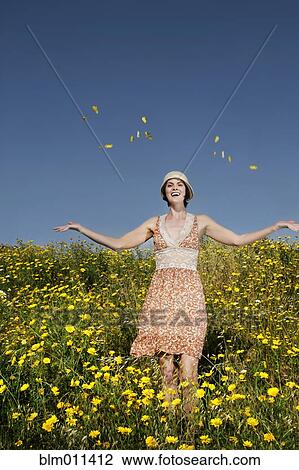 Stock Image - Caucasian woman throwing wildflowers in field. Fotosearch