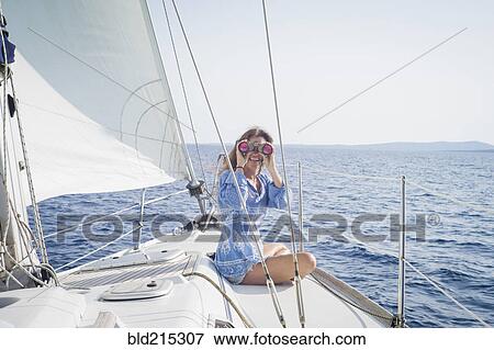 Stock Photo - Caucasian woman using binoculars on boat deck. Fotosearch