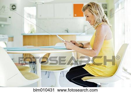 Stock Image - Caucasian woman using digital tablet in dining room. Fotosearch