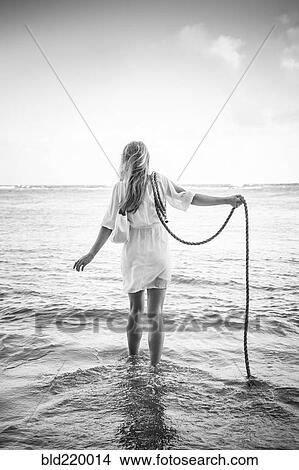 Picture - Caucasian woman wading in ocean waves holding rope. Fotosearch