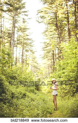 Stock Photo - Caucasian woman walking on grass path in forest. Fotosearch