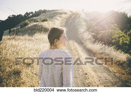 Picture - Caucasian woman walking on rural dirt road. Fotosearch