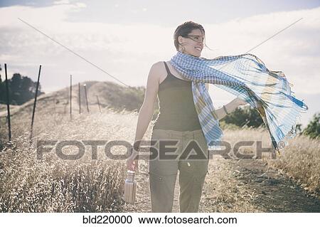 Stock Image - Caucasian woman walking on rural dirt road. Fotosearch