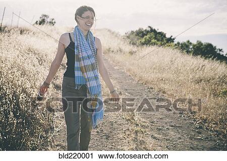 Stock Image - Caucasian woman walking on rural dirt road. Fotosearch