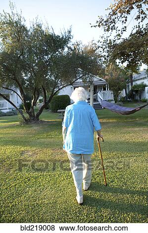 Stock Photo - Caucasian woman walking with cane in backyard. Fotosearch