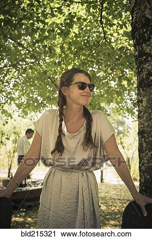 Stock Image - Caucasian woman wearing sunglasses under tree. Fotosearch