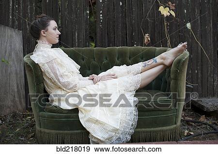 Stock Photo - Caucasian woman wearing vintage gown on backyard sofa. Fotosearch