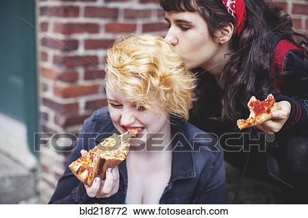 Stock Image - Caucasian women eating pizza outdoors. Fotosearch