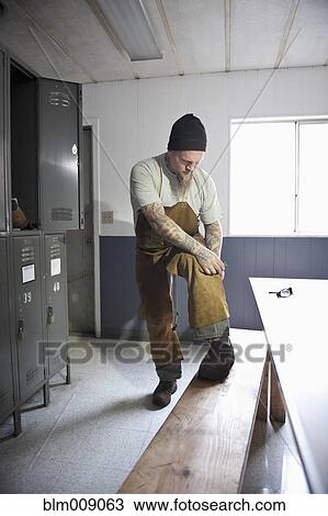 Stock Image - Caucasian worker changing in factory locker room. Fotosearch