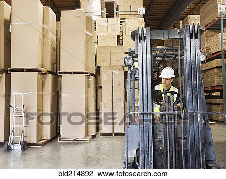 Stock Image - Caucasian worker driving forklift in warehouse. Fotosearch