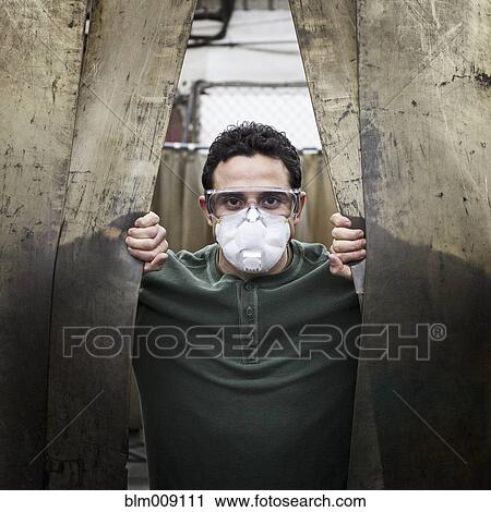 Stock Image - Caucasian worker in protective eyewear and face mask in factory. Fotosearch