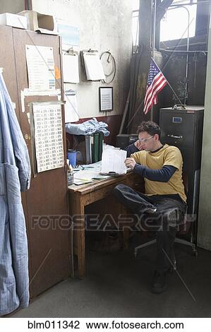 Stock Image - Caucasian worker looking at paperwork in office. Fotosearch