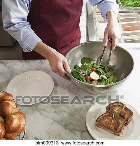 Stock Image - Caucasian worker mixing salad in cafe. Fotosearch