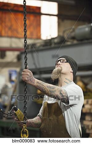 Stock Image - Caucasian worker pulling chain in factory. Fotosearch