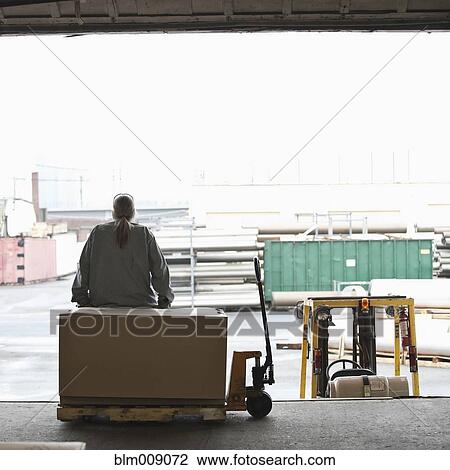 Stock Image - Caucasian worker sitting on loading dock. Fotosearch