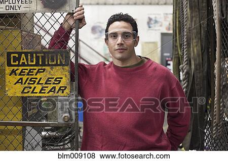 Stock Photo - Caucasian worker standing near fence in factory. Fotosearch