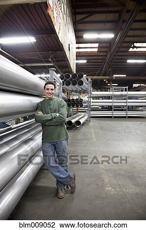 Stock Image - Caucasian worker standing near metal pipes in factory. Fotosearch