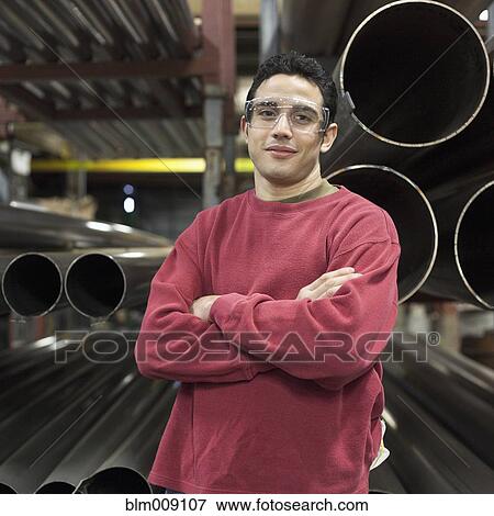 Stock Photo - Caucasian worker standing near metal pipes in factory. Fotosearch