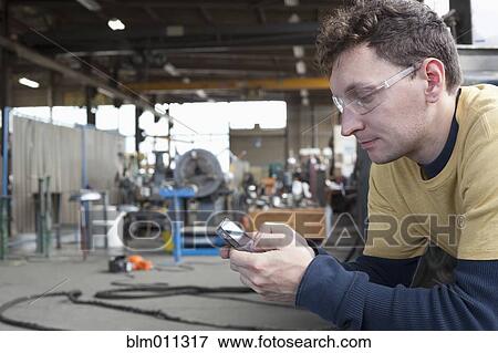 Caucasian worker text messaging on cell phone in warehouse View Large Photo Image Stock Photo - Caucasian worker text messaging on cell phone in warehouse. Fotosearch