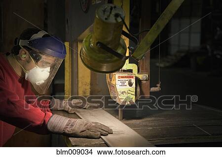 Picture - Caucasian worker using saw in factory. Fotosearch