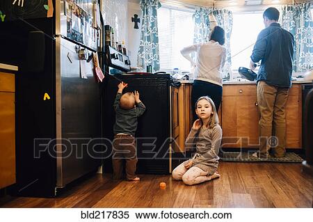 Stock Photography - Children playing as parents cook in kitchen. Fotosearch