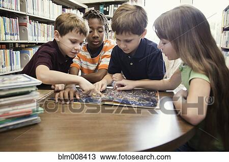 Stock Image - Children reading book together in library. Fotosearch