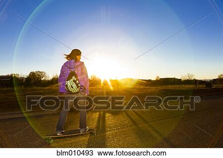 Stock Image - Chinese girl skateboarding on road at sunset. Fotosearch