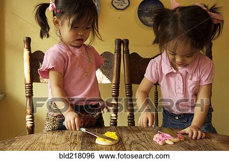 Stock Photograph - Chinese twin girls making cookies at table. Fotosearch