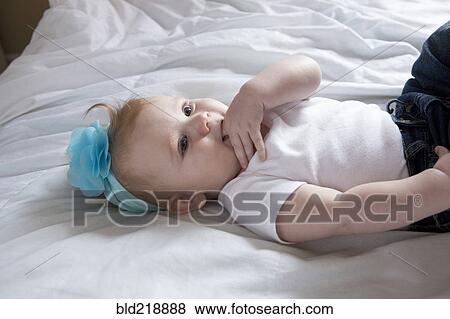 Stock Photo - Close up of baby girl laying on bed. Fotosearch
