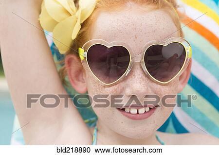 Stock Image - Close up of Caucasian girl wearing heart-shaped sunglasses. Fotosearch