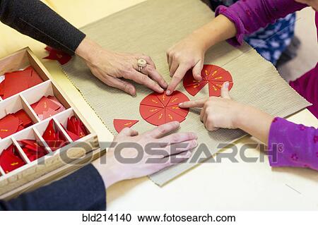 Stock Image - Close up of Caucasian Montessori teacher and student solving puzzle. Fotosearch