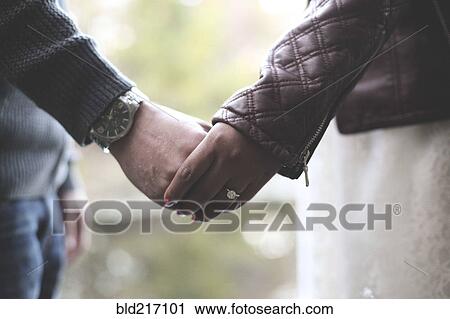 Stock Image - Close up of engaged couple holding hands. Fotosearch