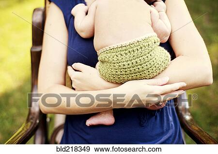 Stock Photo - Close up of girl holding baby in armchair. Fotosearch