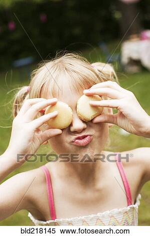 Stock Photography - Close up of girl holding cookies over eyes in backyard. Fotosearch