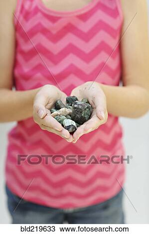 Stock Image - Close up of girl holding handful of stones. Fotosearch