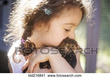 Stock Image - Close up of girl hugging chicken on farm. Fotosearch