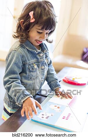 Stock Image - Close up of girl reading book at table. Fotosearch